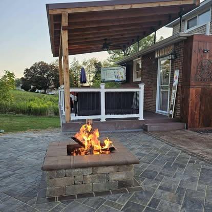 Active stone fire pit on a herringbone paver patio in front of a brick home with a covered deck.