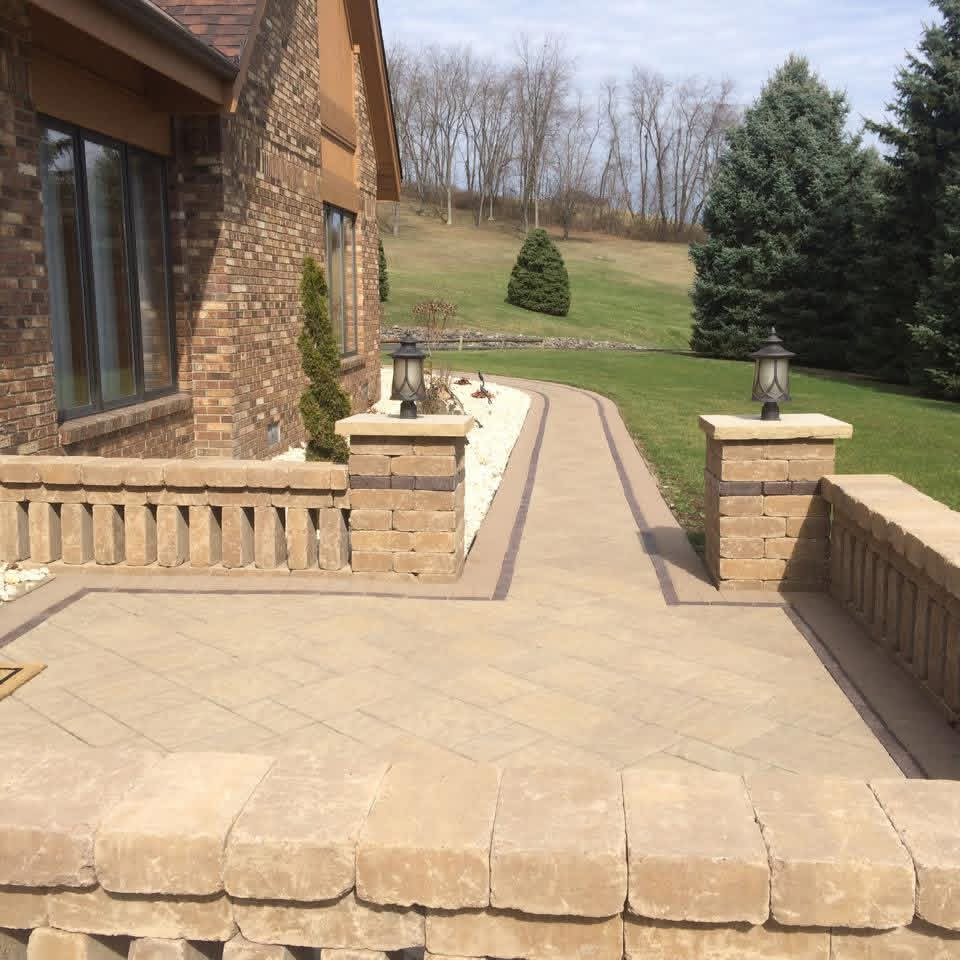 Light paver patio and walkway with low stone walls and black lantern posts leading to a green lawn.