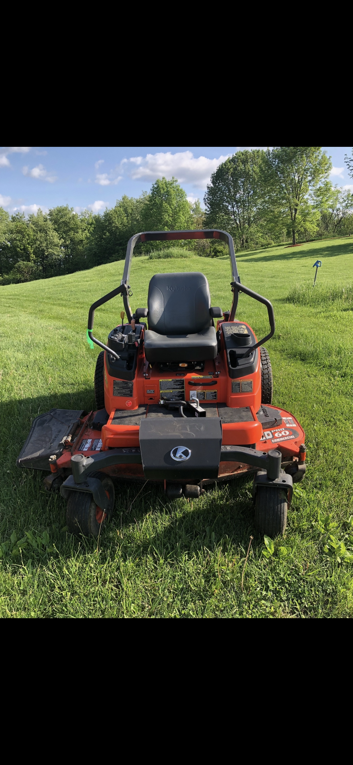 Commercial zero-turn mower parked on a green lawn with trees in the background.