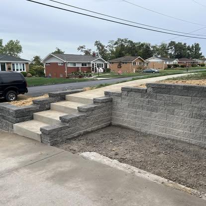 New concrete steps and tiered gray block retaining wall connecting a driveway to the sidewalk.