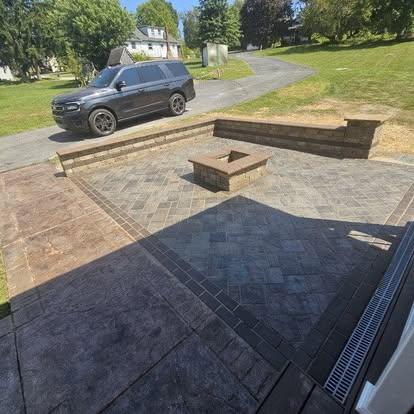 Paver patio with square stone fire pit, L-shaped retaining wall, and stamped concrete border.