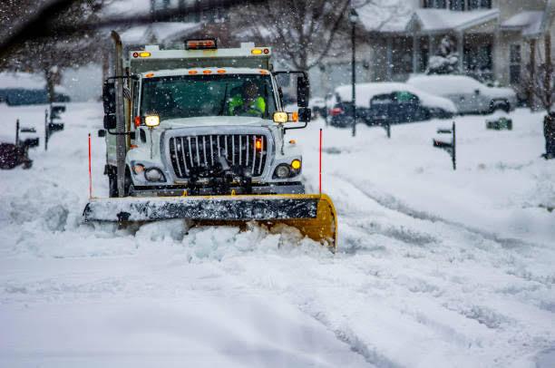 Professional snow plow truck clearing a residential street during active snowfall